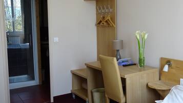 Habitación de hotel con un escritorio de madera, una silla, una lámpara, un cubo de basura pequeño, una mesita de noche con lámpara y una cama.