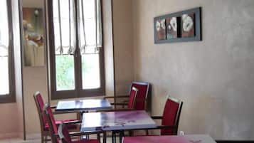 A dining area with tables and chairs, a window with curtains, and a wall with a framed artwork.