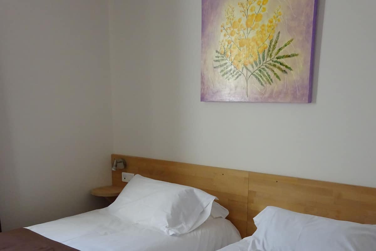 A hotel room with two beds, each with white linens and brown headboards.