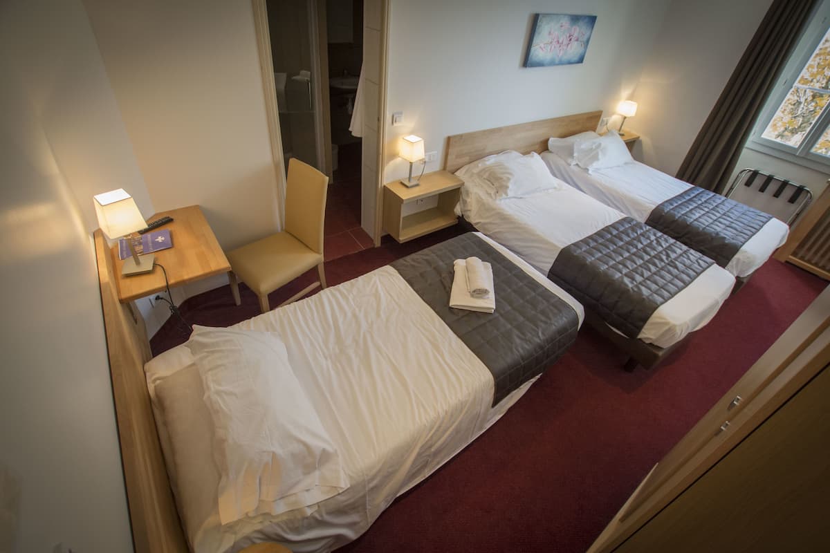 A hotel room with two beds, a chair, a nightstand with a lamp, and a painting on the wall.