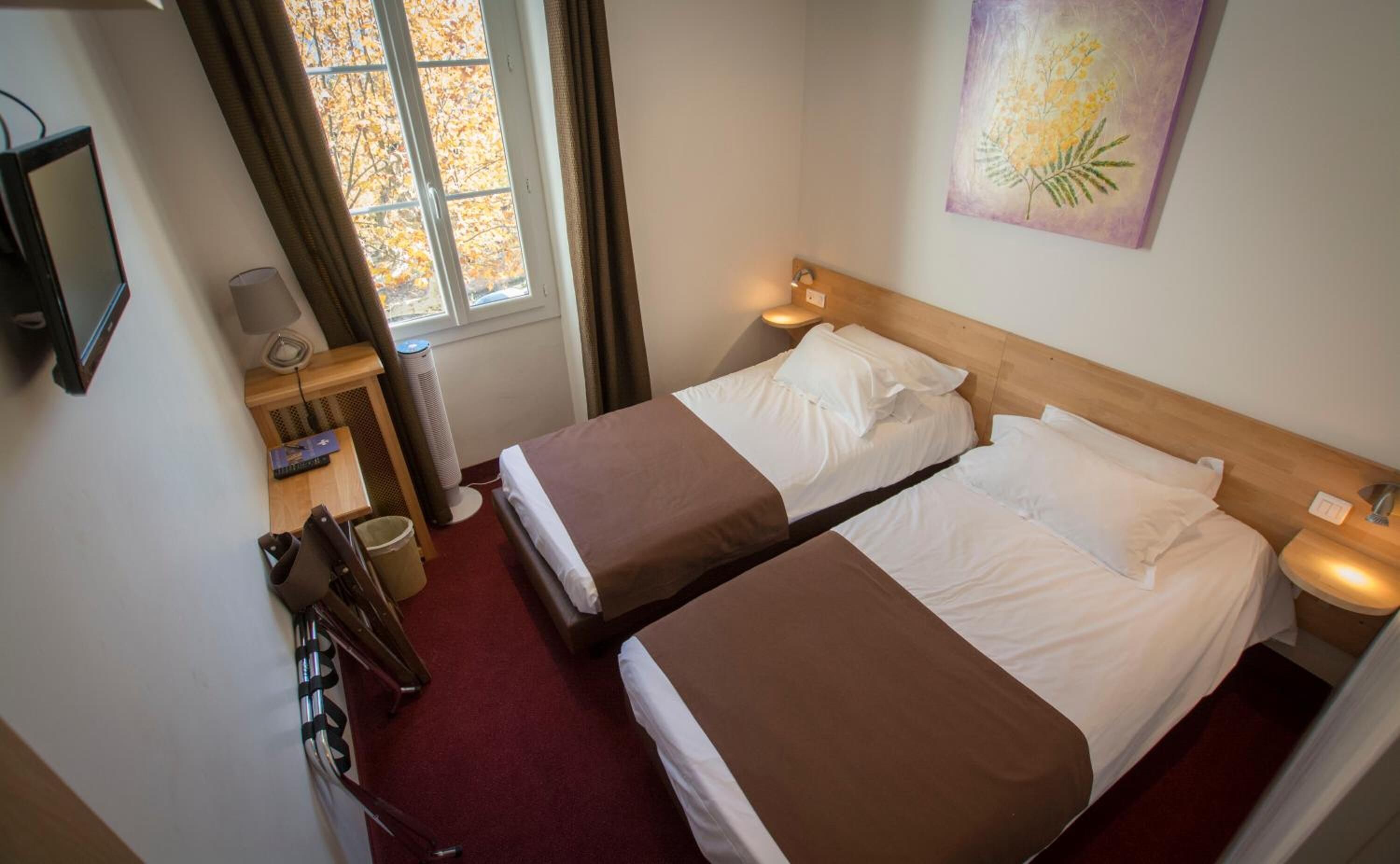 Habitación de hotel con dos camas, televisión, escritorio con lámpara y ventana con cortinas.