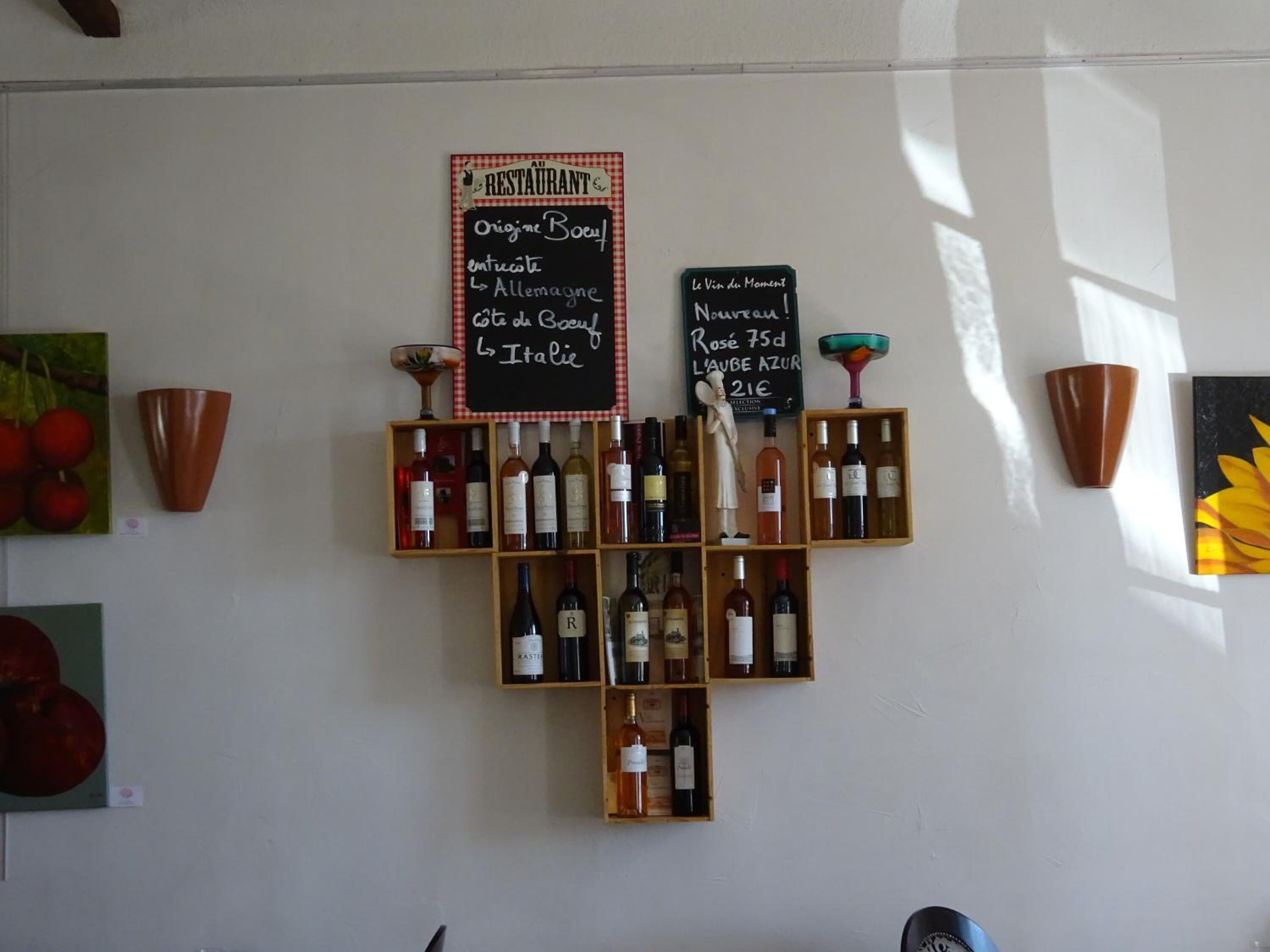 Un présentoir à bouteilles de vin, avec des bouteilles et deux panneaux noirs indiquant l’origine des vins.