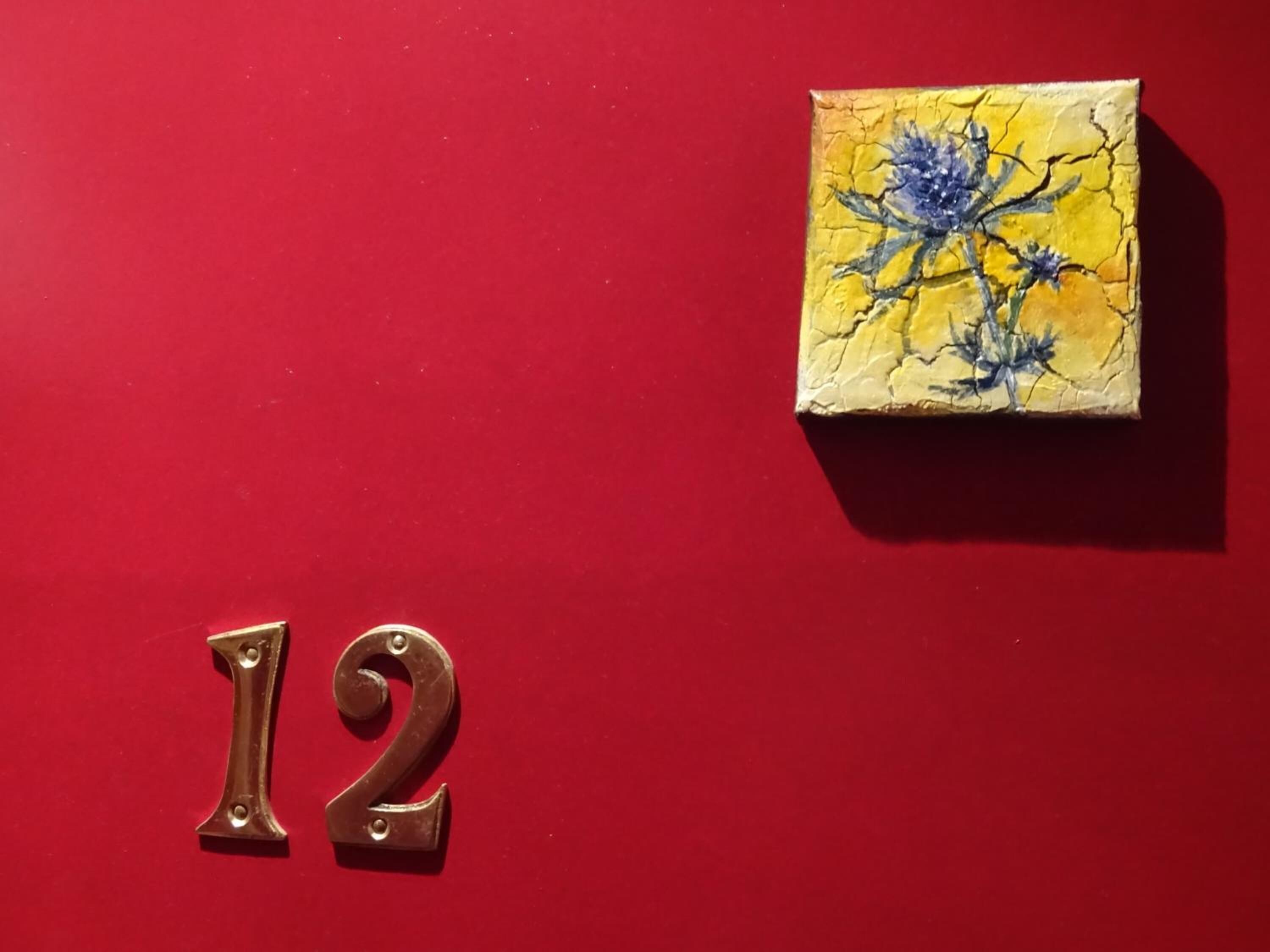 Una pared roja con el número 12 y una pequeña pintura de flores.