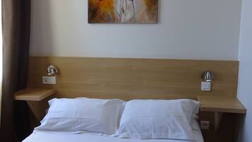 Una habitación de hotel con una cama, dos mesitas de noche y un cuadro de flores rojas en la pared.