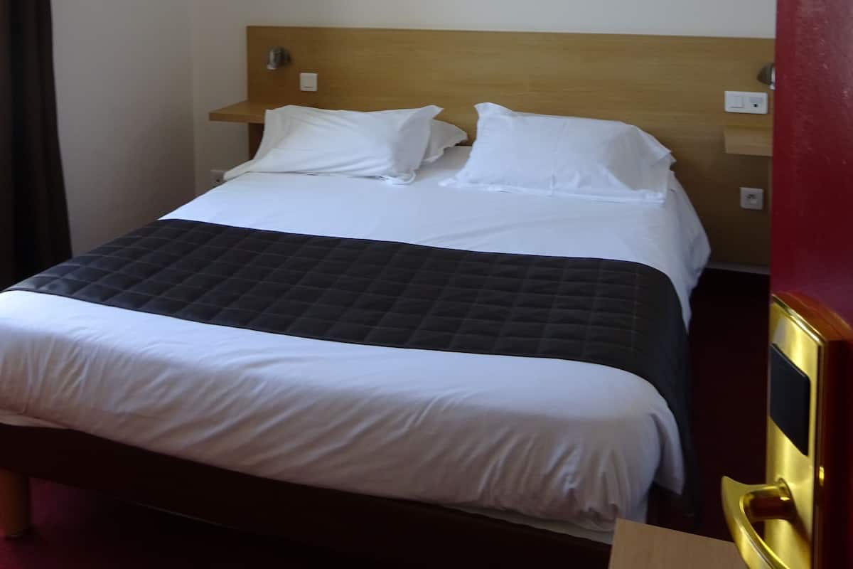 A hotel room with a bed, a painting of yellow flowers on the wall, and a wooden headboard.