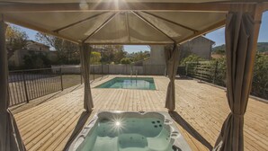 Una terraza de madera con un jacuzzi bajo una toldo.