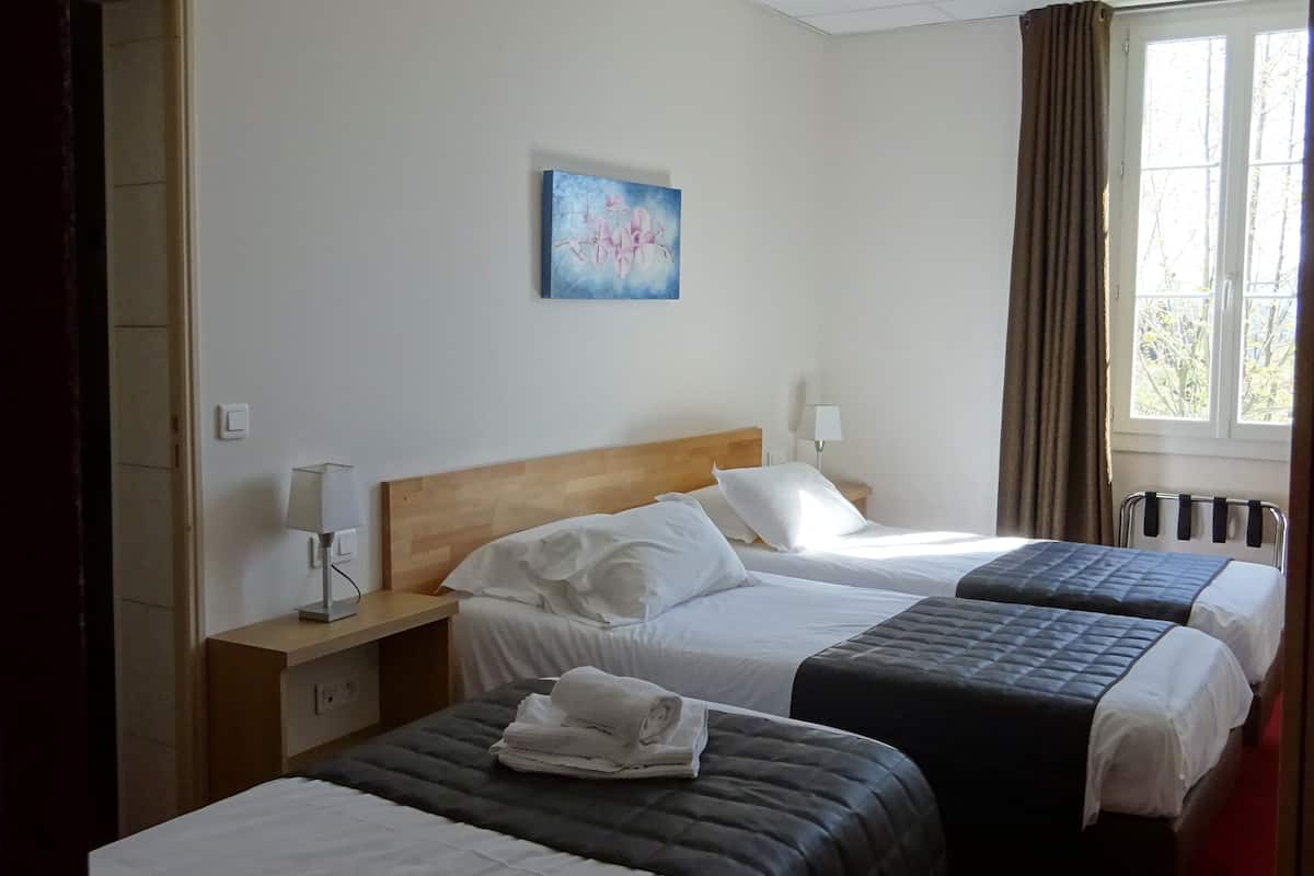 A hotel room with three beds, a wooden headboard, a painting on the wall, and a window with curtains.