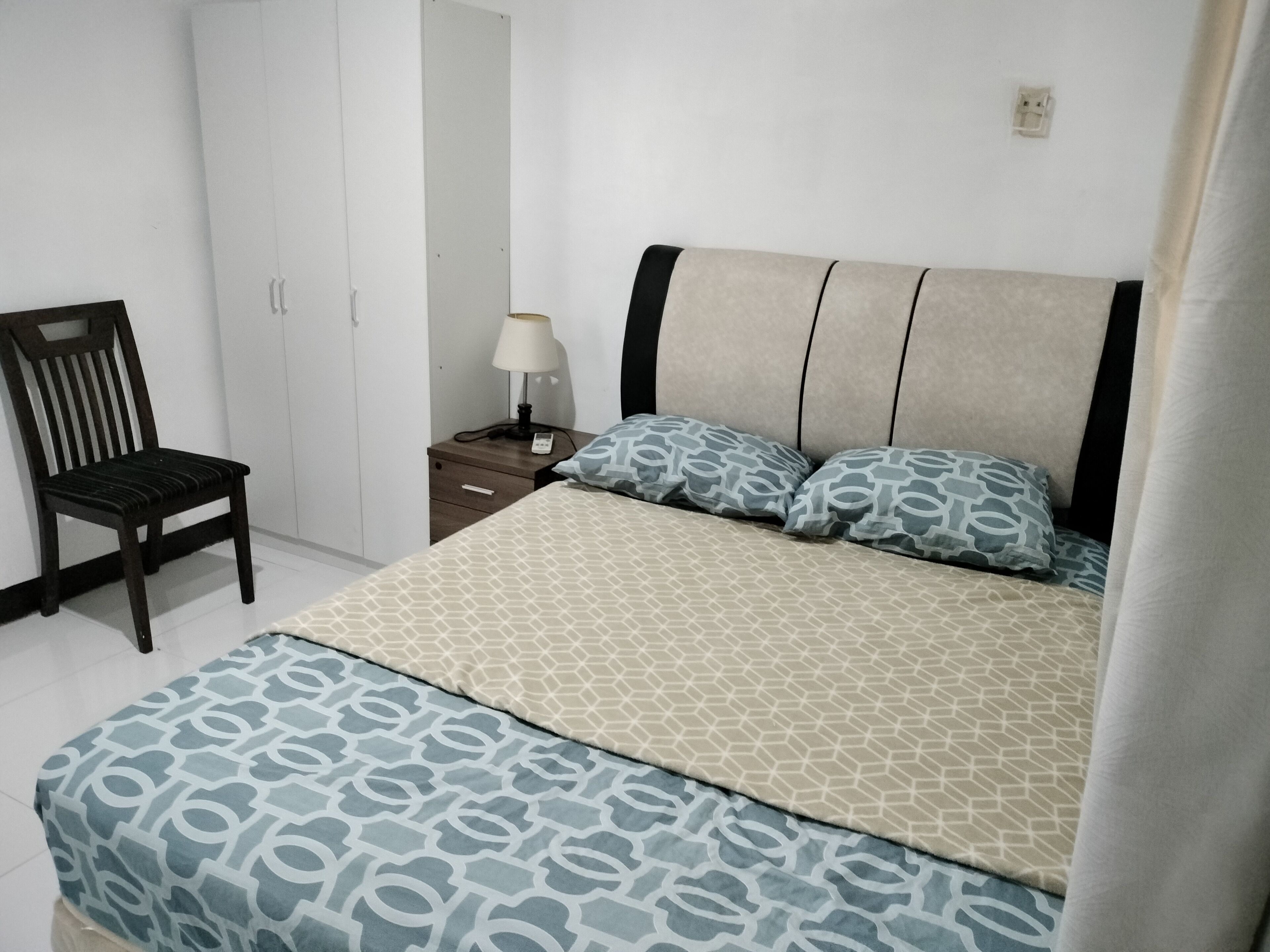 Een slaapkamer met een bed, een stoel, een nachtkastje en een lamp.