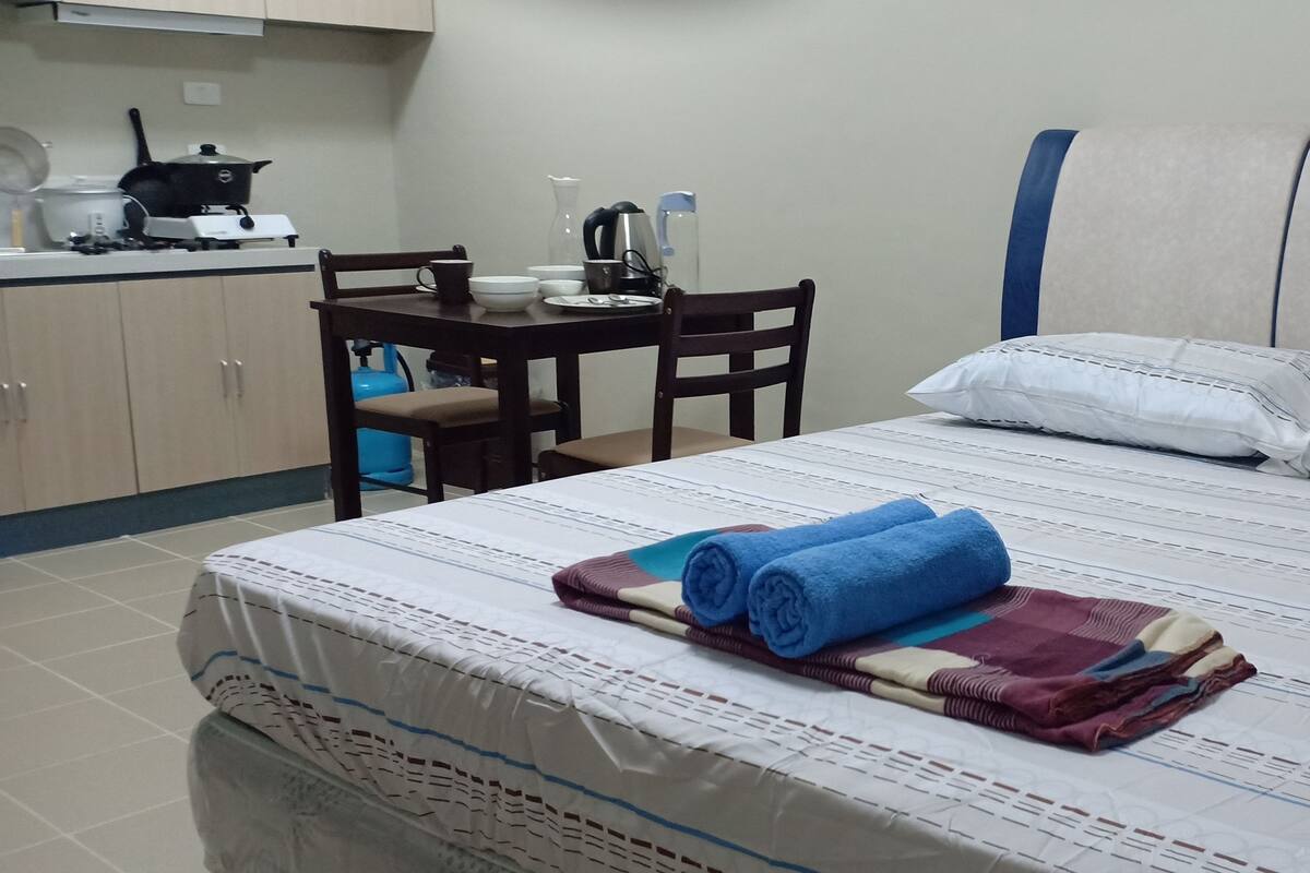 Une chambre d’hôtel comprenant un lit, une petite table avec des chaises, un coin cuisine et un distributeur d’eau.