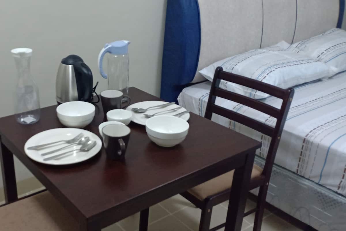 Une table à manger bien dressée, avec des assiettes, des couverts et une bouilloire, dans une pièce qui contient un lit et une chaise.