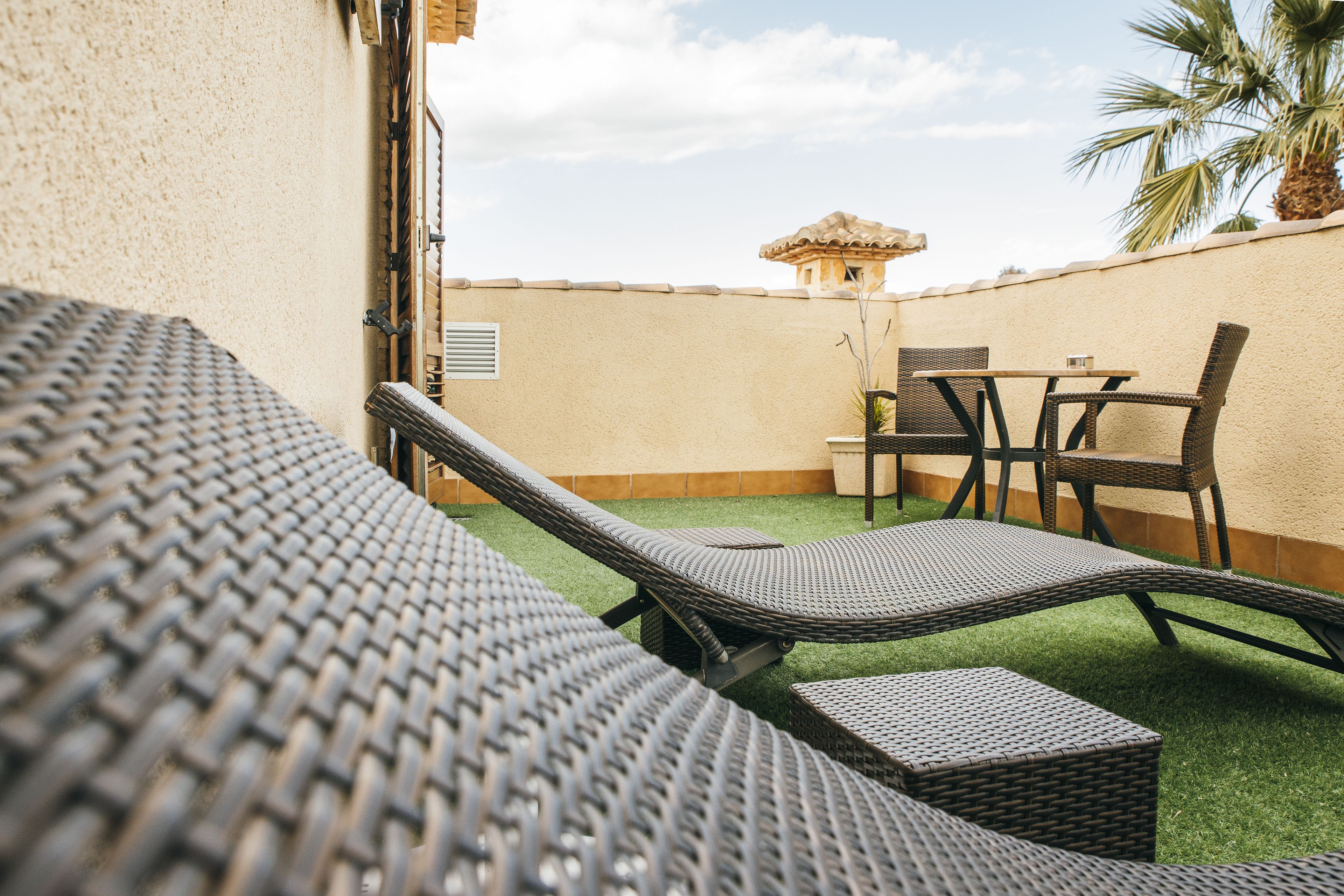 Un patio con sillones de mimbre, una mesita y una planta en maceta.