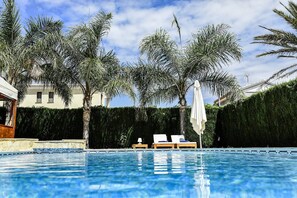 Una piscina con sillones de descanso y palmeras.