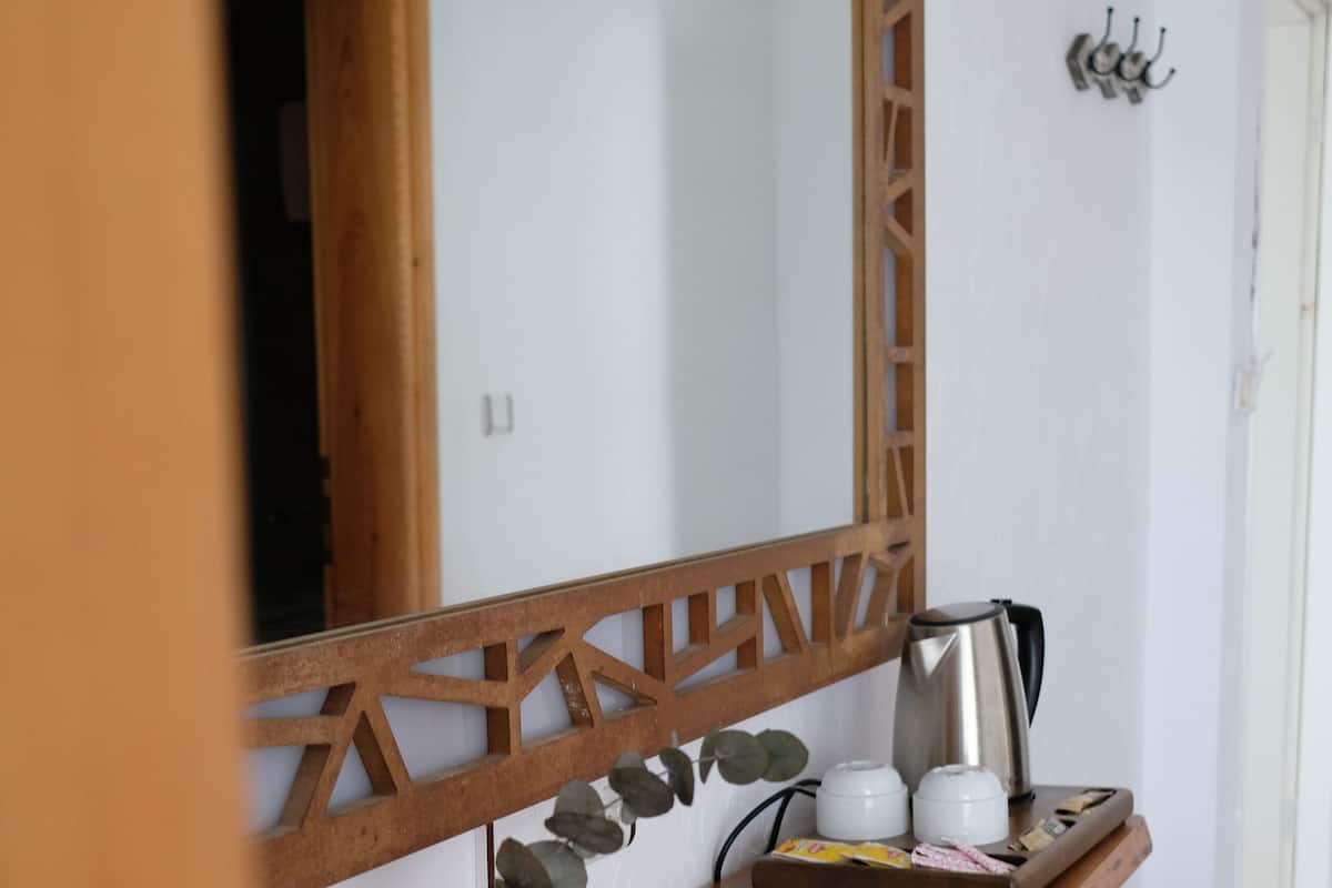 Una kitchenette con encimera de madera, una tetera de acero inoxidable, dos tazas blancas, una botella y una bandeja con una bolsita de té y un sobre de azúcar.