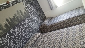A room with patterned bedding, a cityscape artwork on the wall, and a window with curtains. - Camelot (Villarrobledo)