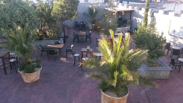 An outdoor patio area with multiple tables and chairs, surrounded by potted plants. - Camelot (Villarrobledo)