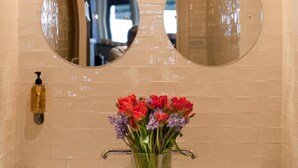 A bathroom with two round mirrors, a white sink, and a vase with flowers. - The Tommyfield (London)