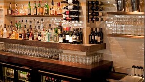 A bar area with shelves of various liquor bottles, glasses, and a hanging light fixture. - The Tommyfield (London)