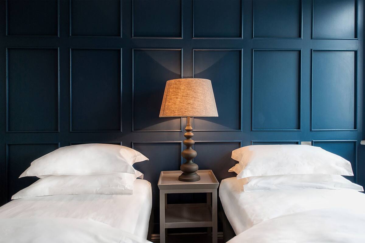 A hotel room with two beds, a nightstand, and a lamp.