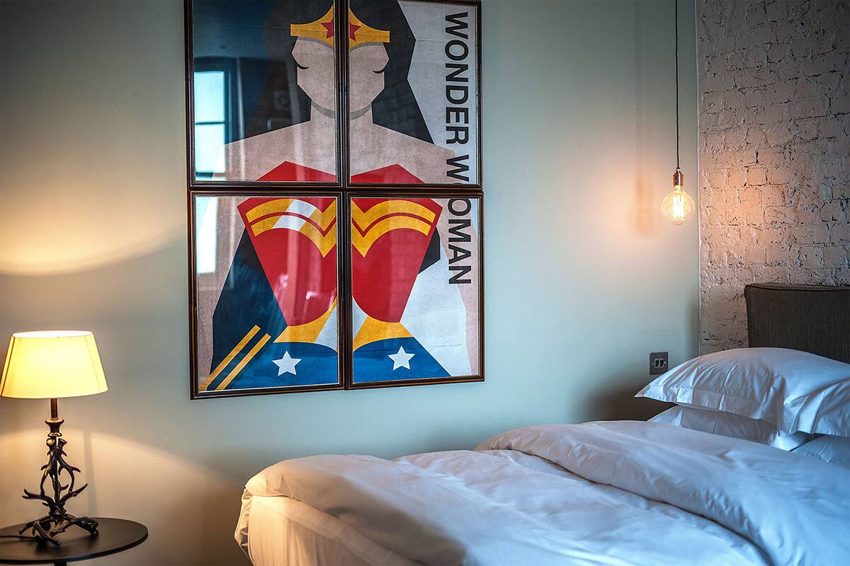 A hotel room with a bed, a lamp, and a wall with a Wonder Woman poster.
