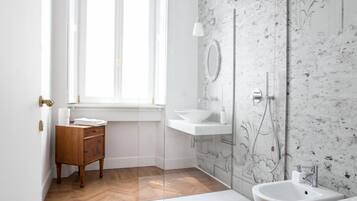 Een moderne badkamer met een houten vloer, witte sanitair en een kroonluchter, plus een raam.