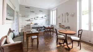 A spacious dining area with a wooden table and chairs, a sofa, and a kitchen with white cabinets and a herringbone floor pattern. - B&B La Foresteria (Milan)