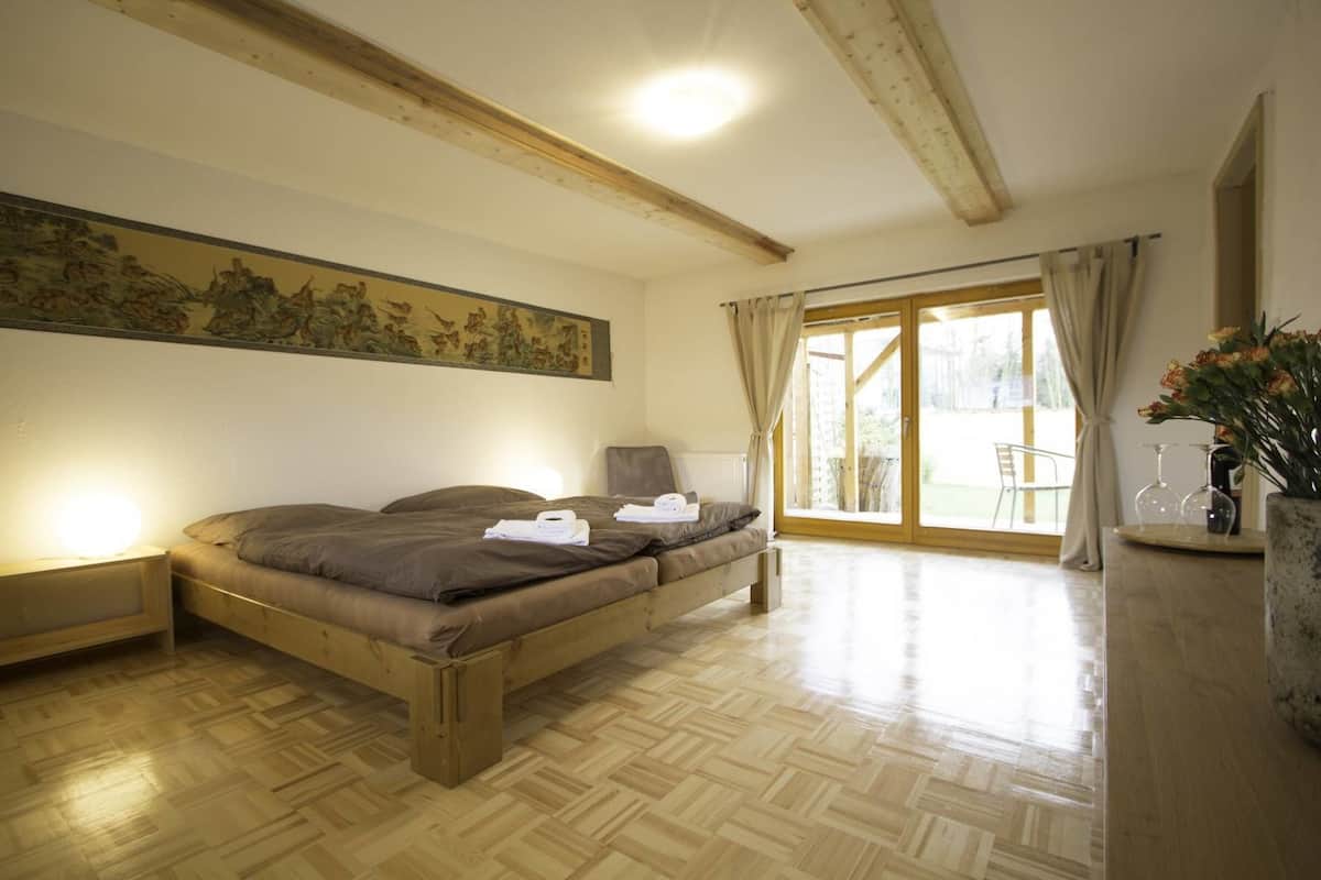 Ein Schlafzimmer mit einem hölzernen Bett, einem Nachttisch, einem großen Fenster mit Vorhängen und einem Bild an der Wand.