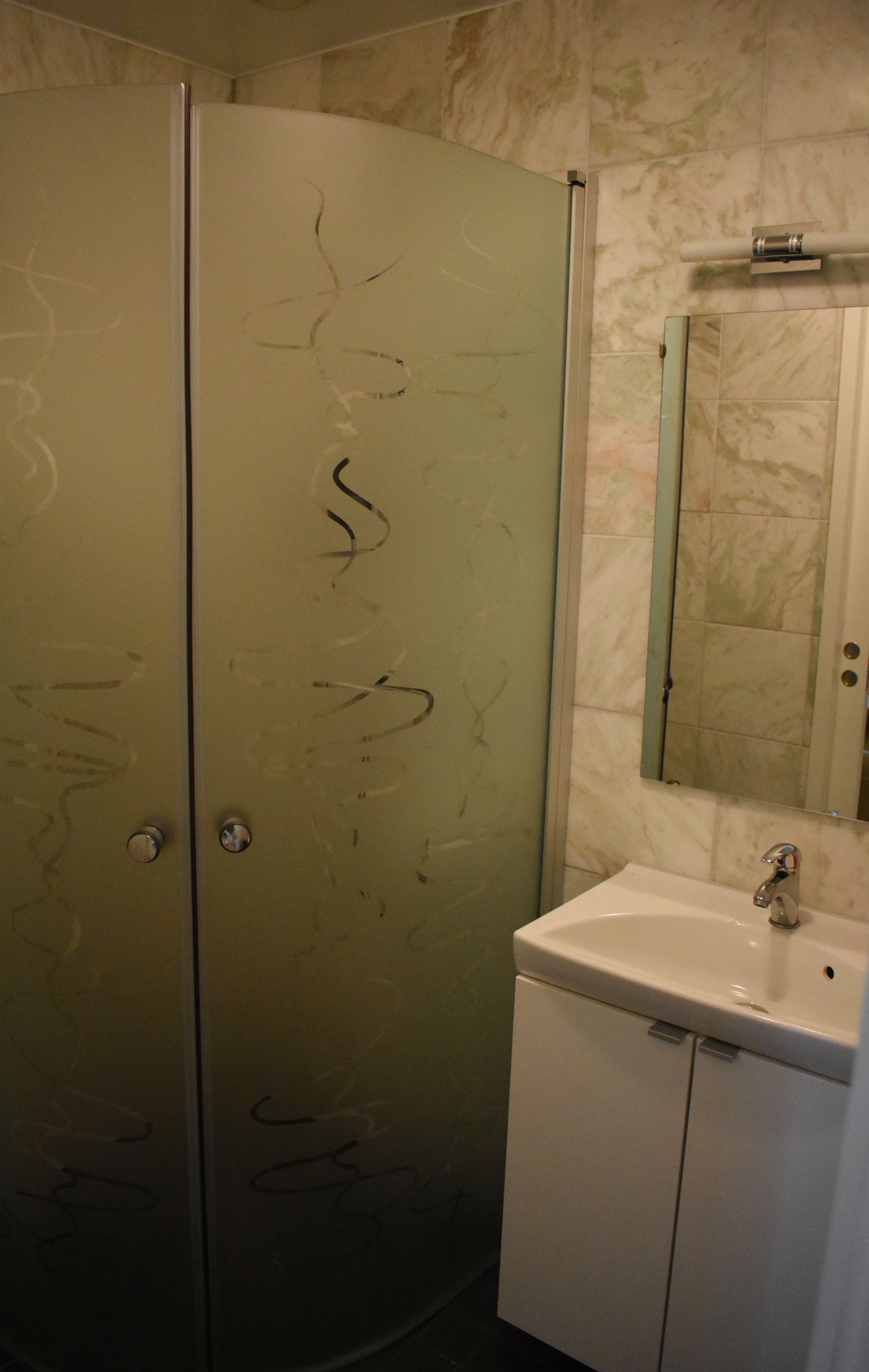 A bathroom with a white sink, a mirror above it, and a glass shower enclosure with graffiti on the door.
