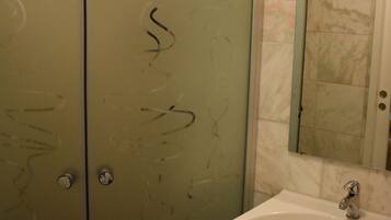 A bathroom with a white sink, a mirror above it, and a glass shower enclosure with graffiti on the door.