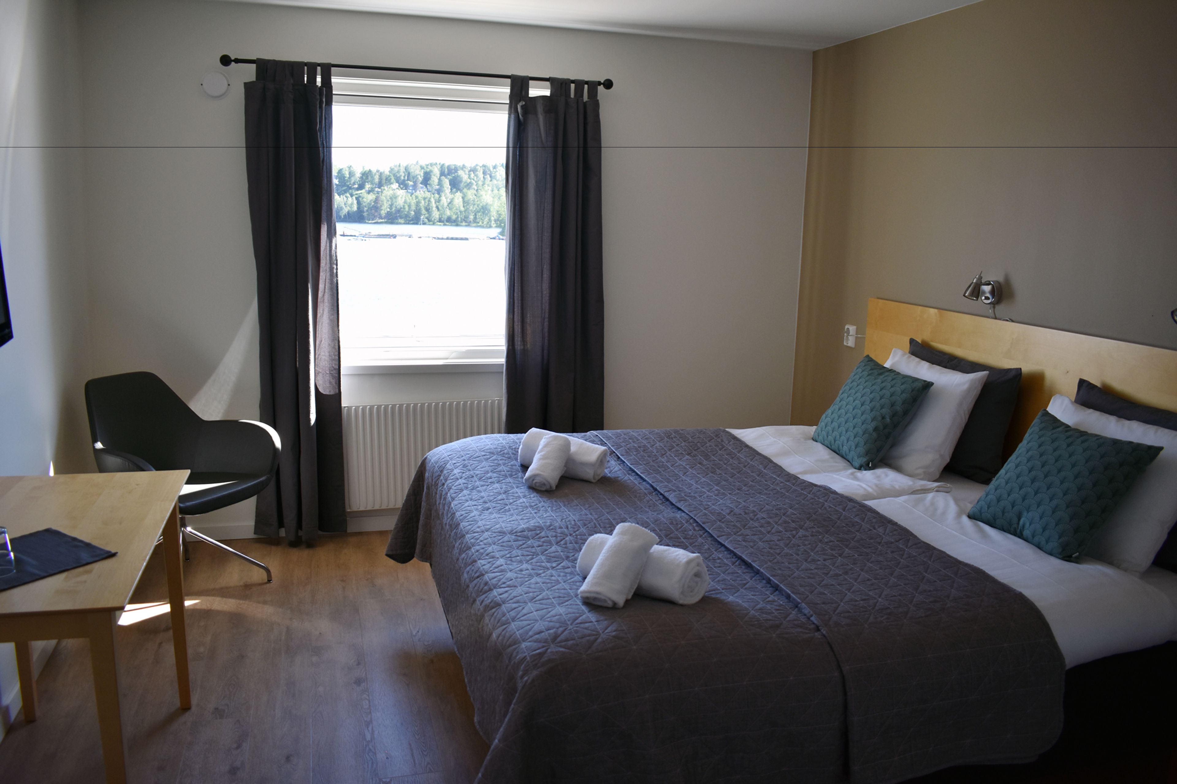 Una habitación de hotel con una cama, una silla, una mesa y un ventanal con cortinas.