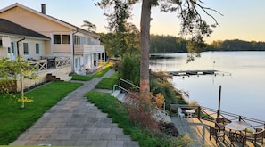 A lakeside property with a covered patio, a wooden deck, and a stone pathway leading to the house. - Håveruds Hotell (Håverud)