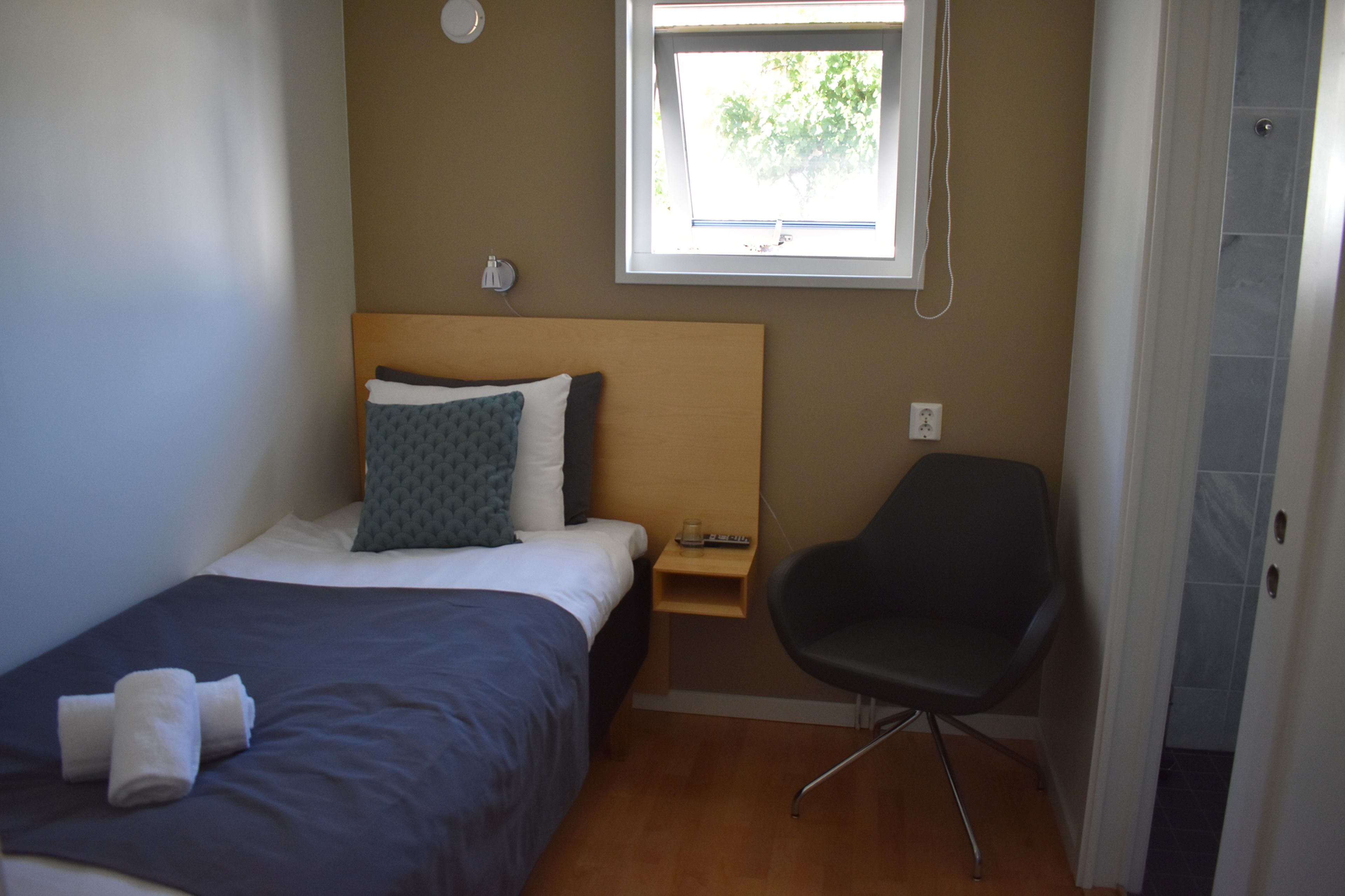 Una habitación de hotel con cama, una silla, una mesita de noche y un ventanal.