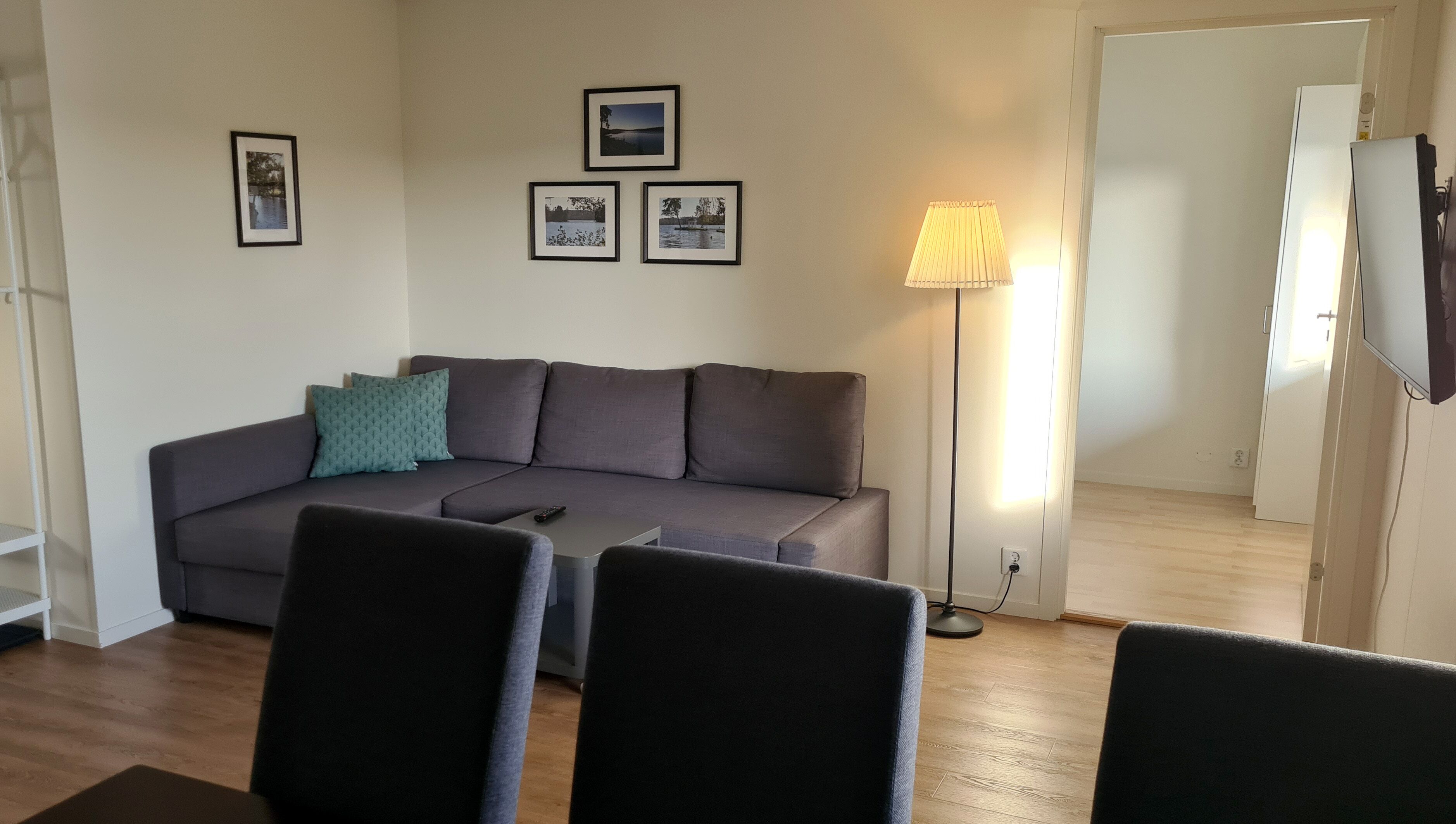 A living room with a grey sofa, a standing lamp, and framed pictures on the wall.