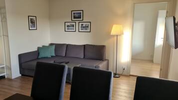A living room with a grey sofa, a standing lamp, and framed pictures on the wall.