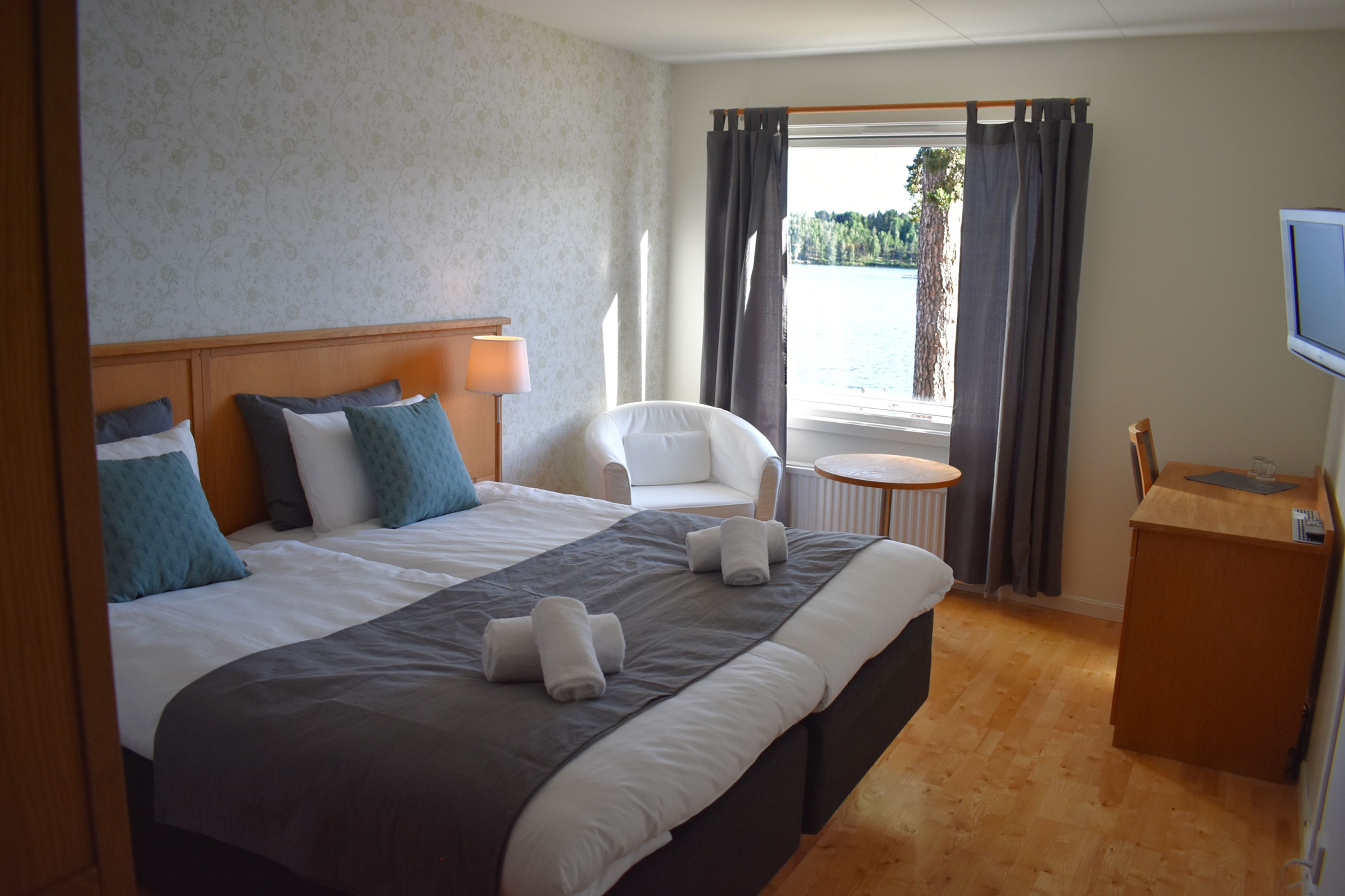 A hotel room with a large bed, a chair, a small table, and a TV.