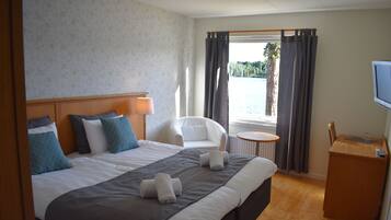 A hotel room with a large bed, a chair, a small table, and a TV.