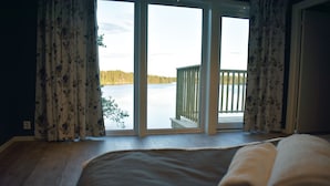 Een slaapkamer met een groot raam dat uitkijkt over een meer en een houten terras.