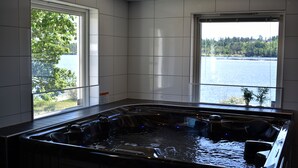 Een wellnessruimte met een jacuzzi, grote ramen en uitzicht op een meer.