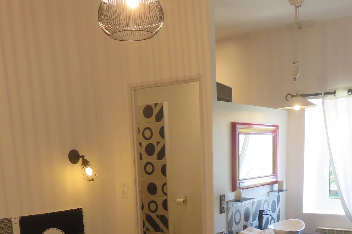 A bedroom with a large bed, a bedside table, a mirror, a window, and a bathroom with a sink and towel rack.