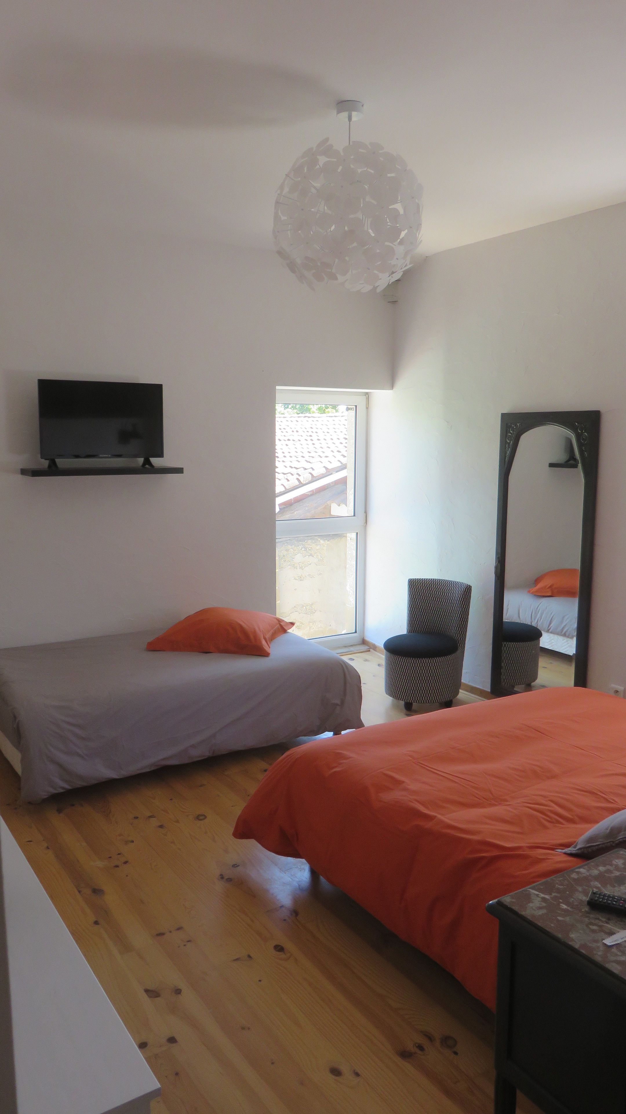 Un dormitorio con dos camas, televisión, espejo y lámpara colgante.