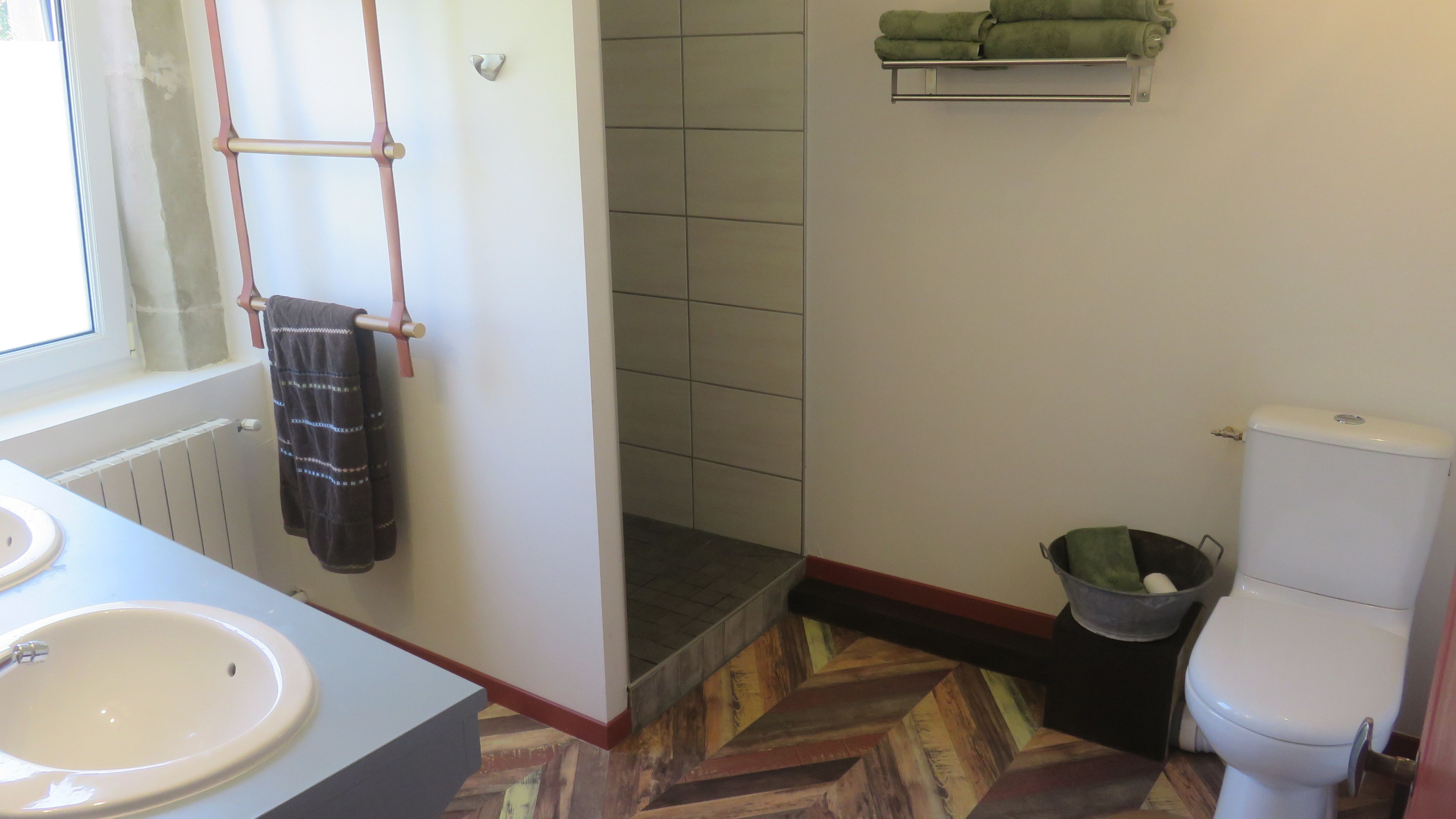 A bathroom with a white sink, a toilet, a shower area, and a wooden floor.
