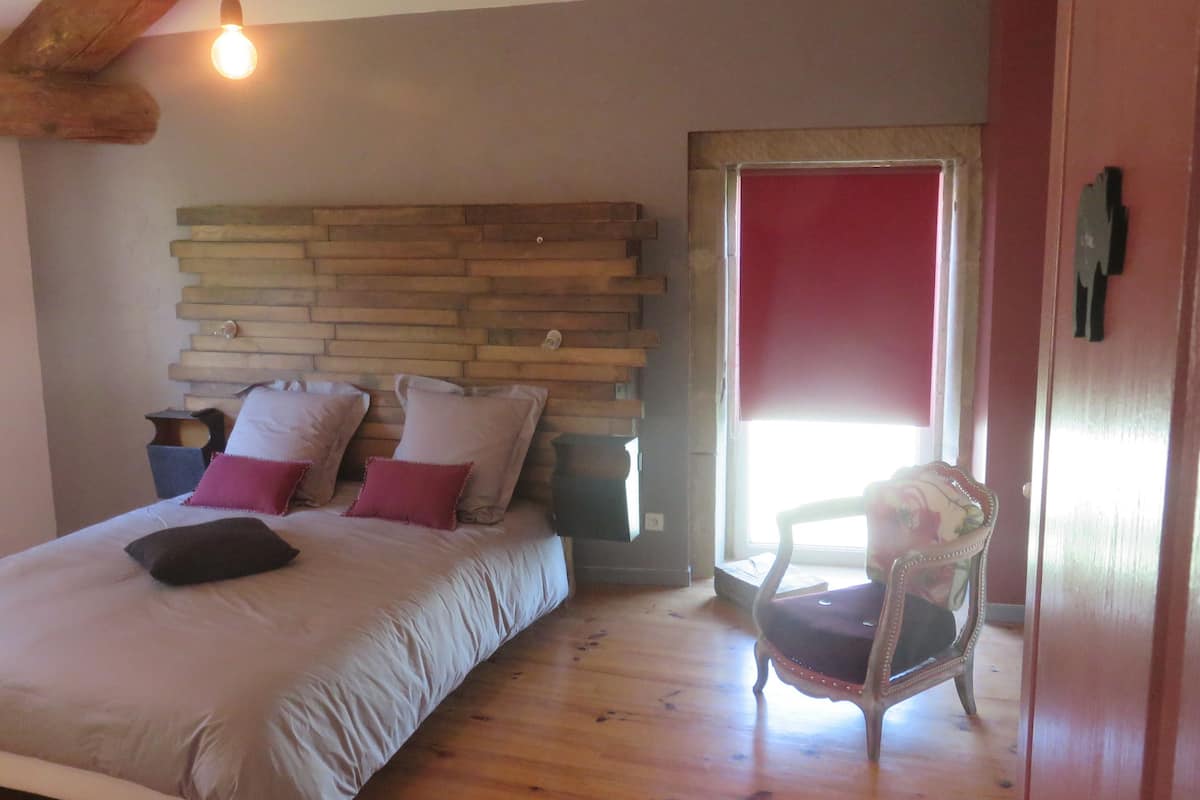 A bedroom with a wooden headboard, a bed with multiple pillows, a chair, and a window with a red blind.