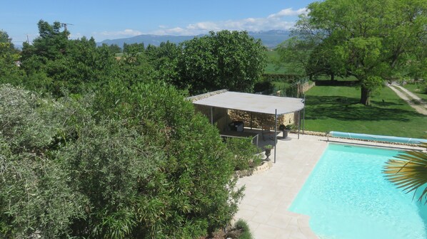 Un área de piscina con zona de estar cubierta, rodeada de exuberante vegetación y vistas a montañas distantes.