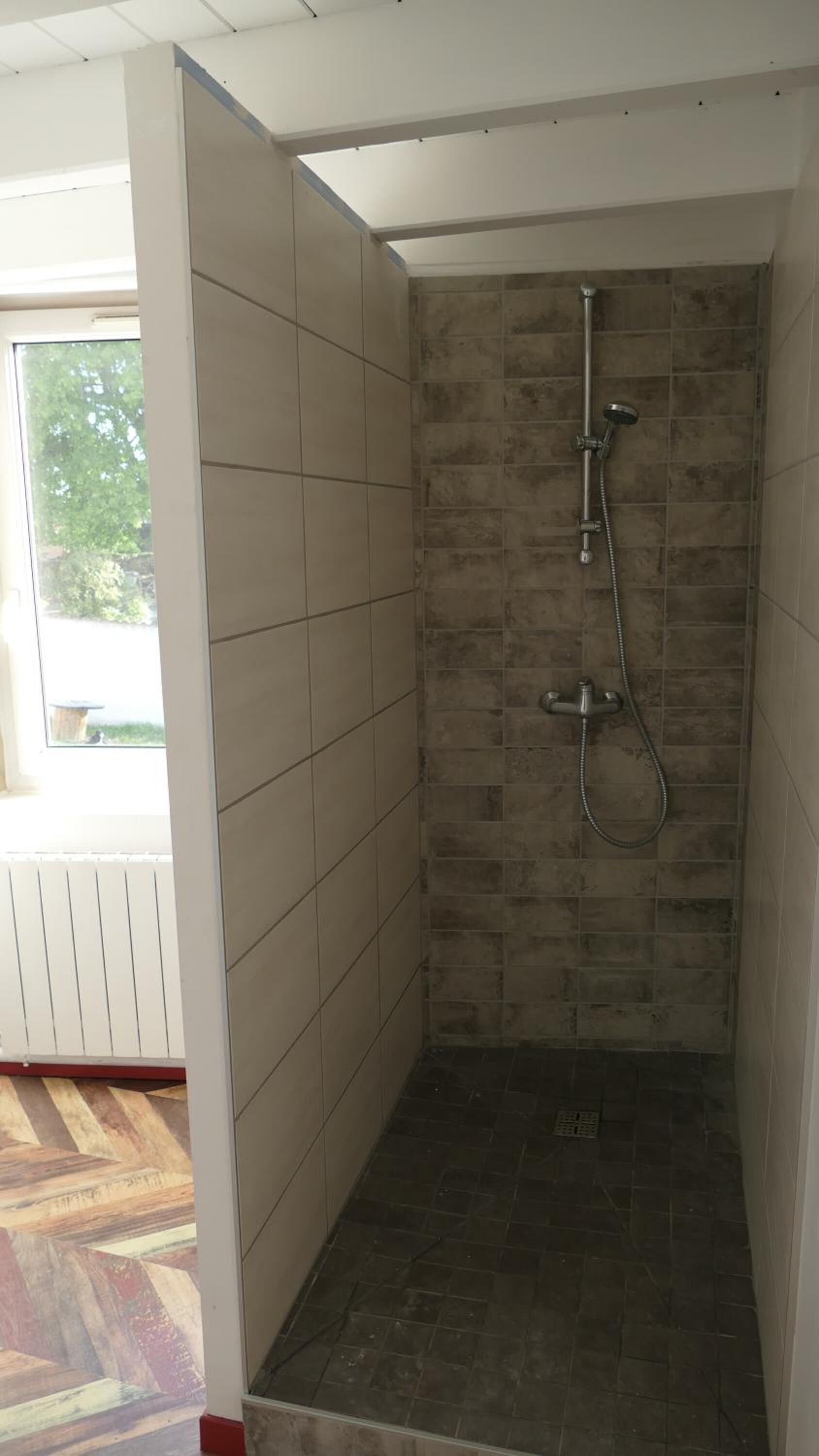 A shower with a tiled wall and floor, a handheld showerhead, and a wall-mounted faucet.
