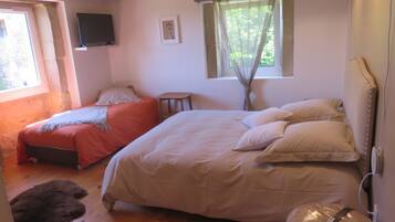 A bedroom with two beds, a window with curtains, a small table, and a wall-mounted TV.