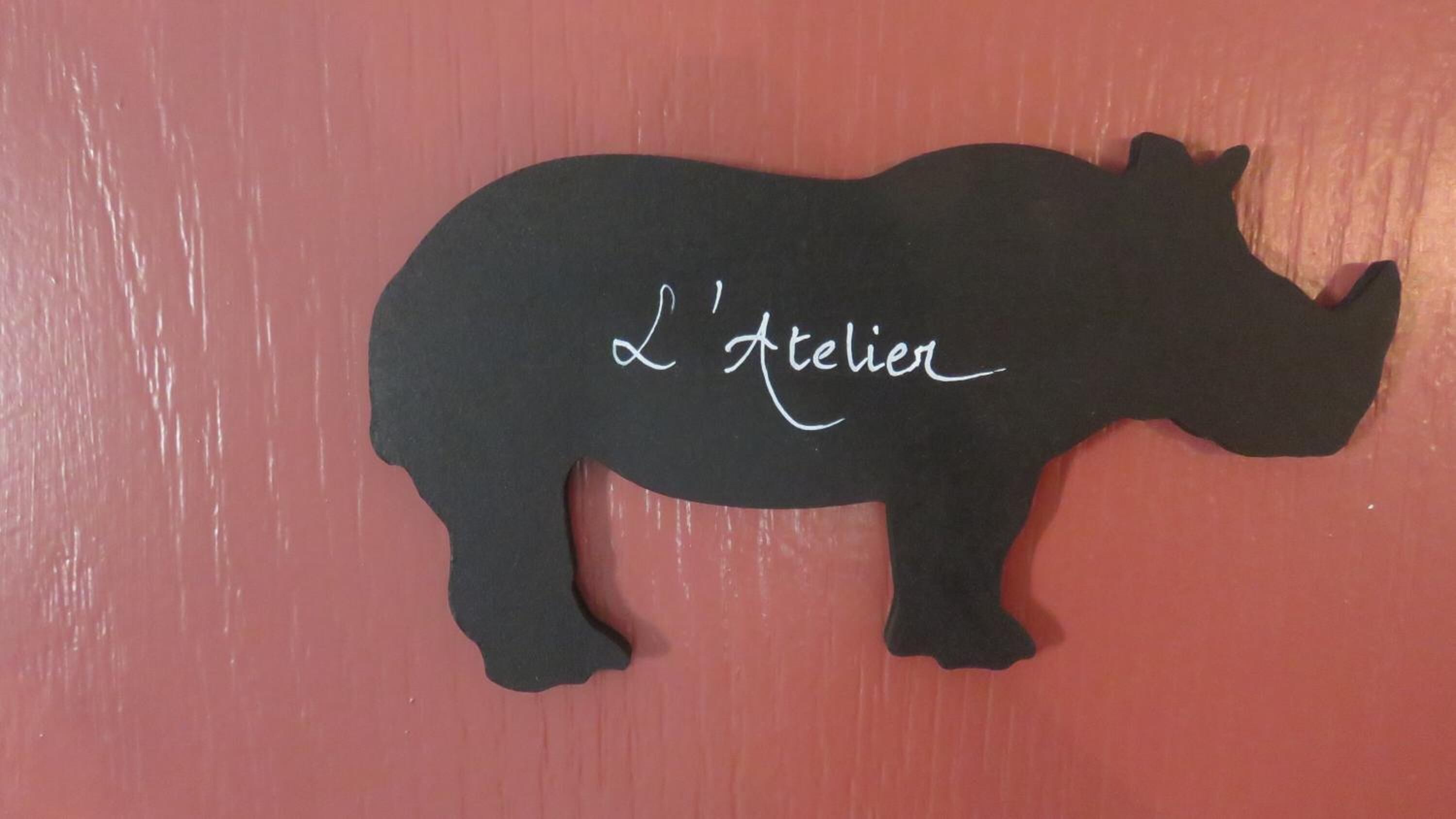 En siluett av ett noshörn med texten ”L’atelier” på en röd bakgrund.
