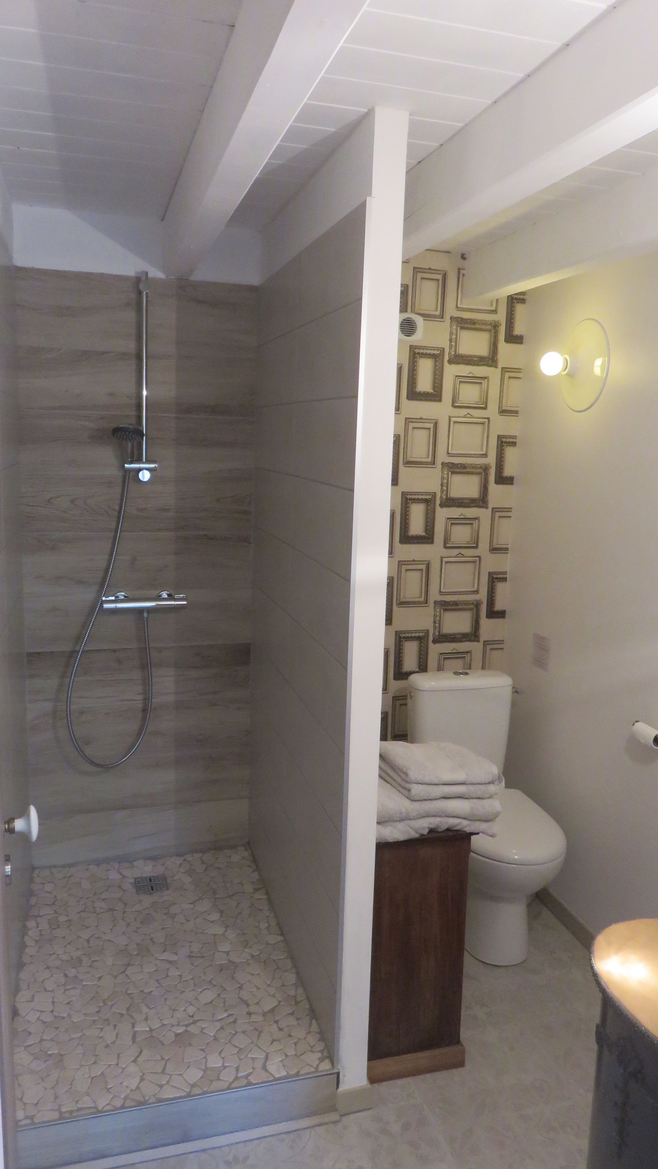 A bathroom with a shower, toilet, and a wall with framed pictures.
