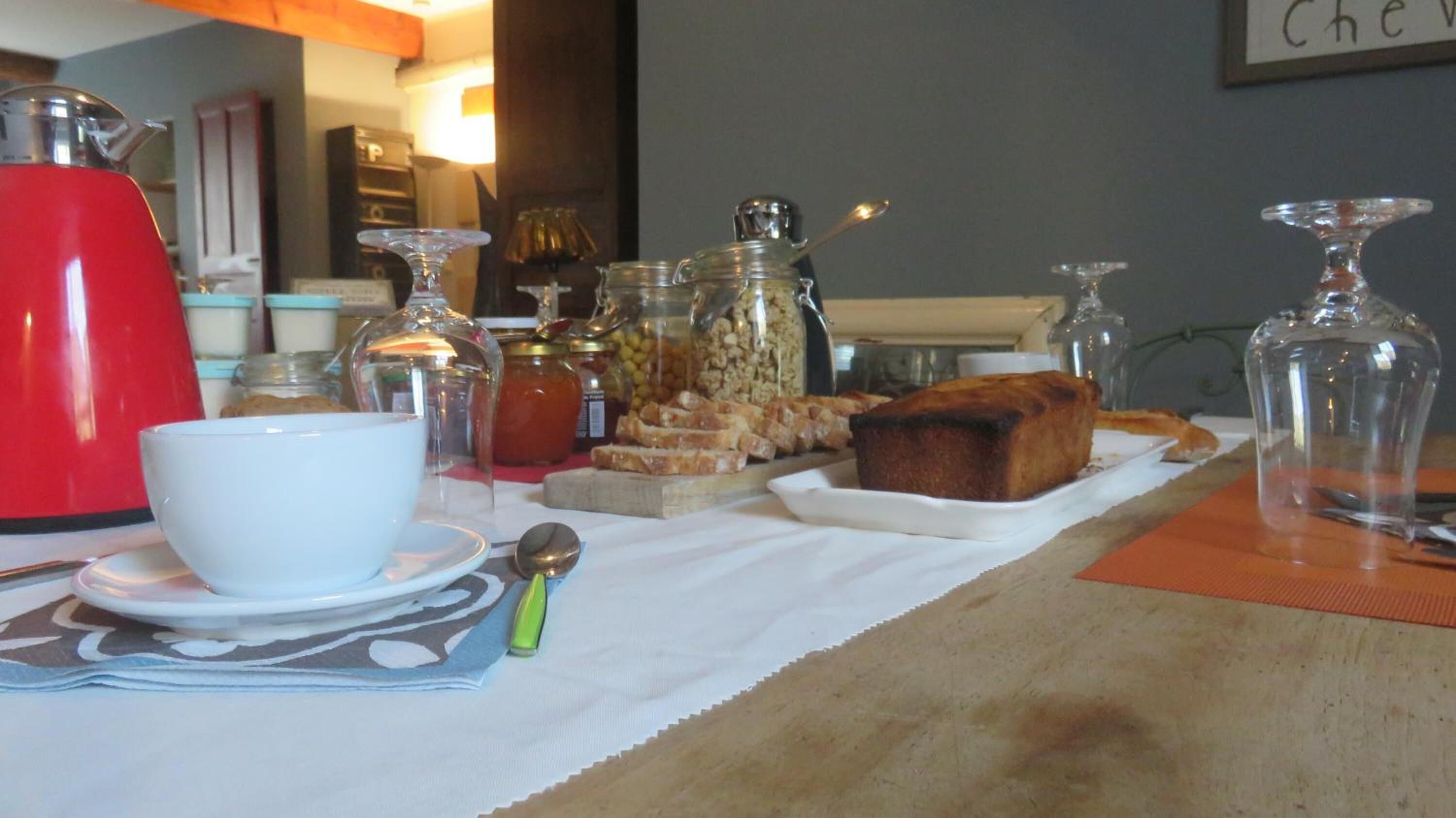 A breakfast table with a cup, a spoon, a loaf of bread, and various jars of spreads and condiments.