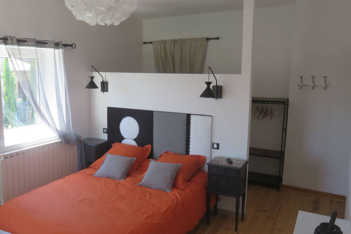 A bedroom with a bed, bedside tables, a window with curtains, a ceiling light, and a wall-mounted shelf.