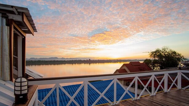 Una terraza de madera con barandal blanco que da a un lago tranquilo al atardecer.