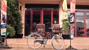 Una bicicleta estacionada frente a un edificio con un cartel, plantas en macetas y un banco de madera.